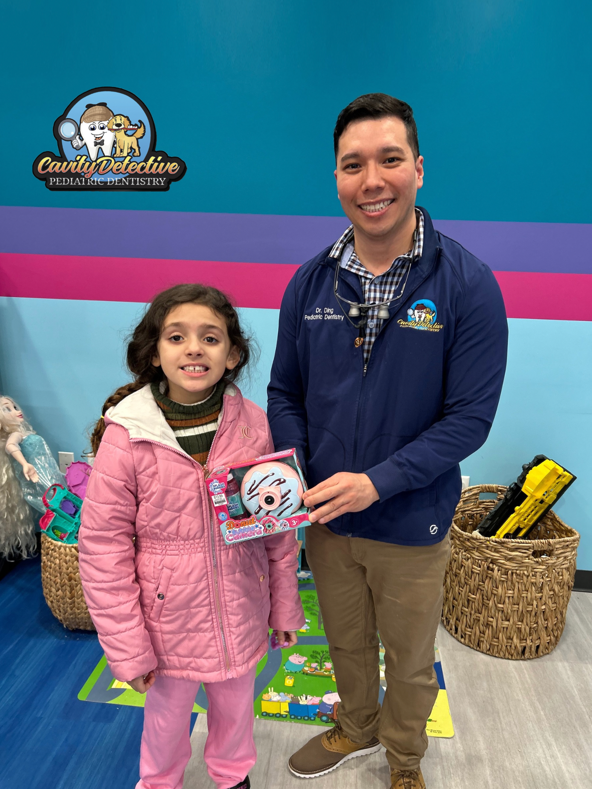 Two people smiling at a colorful event booth, holding a small sign and a plush toy.