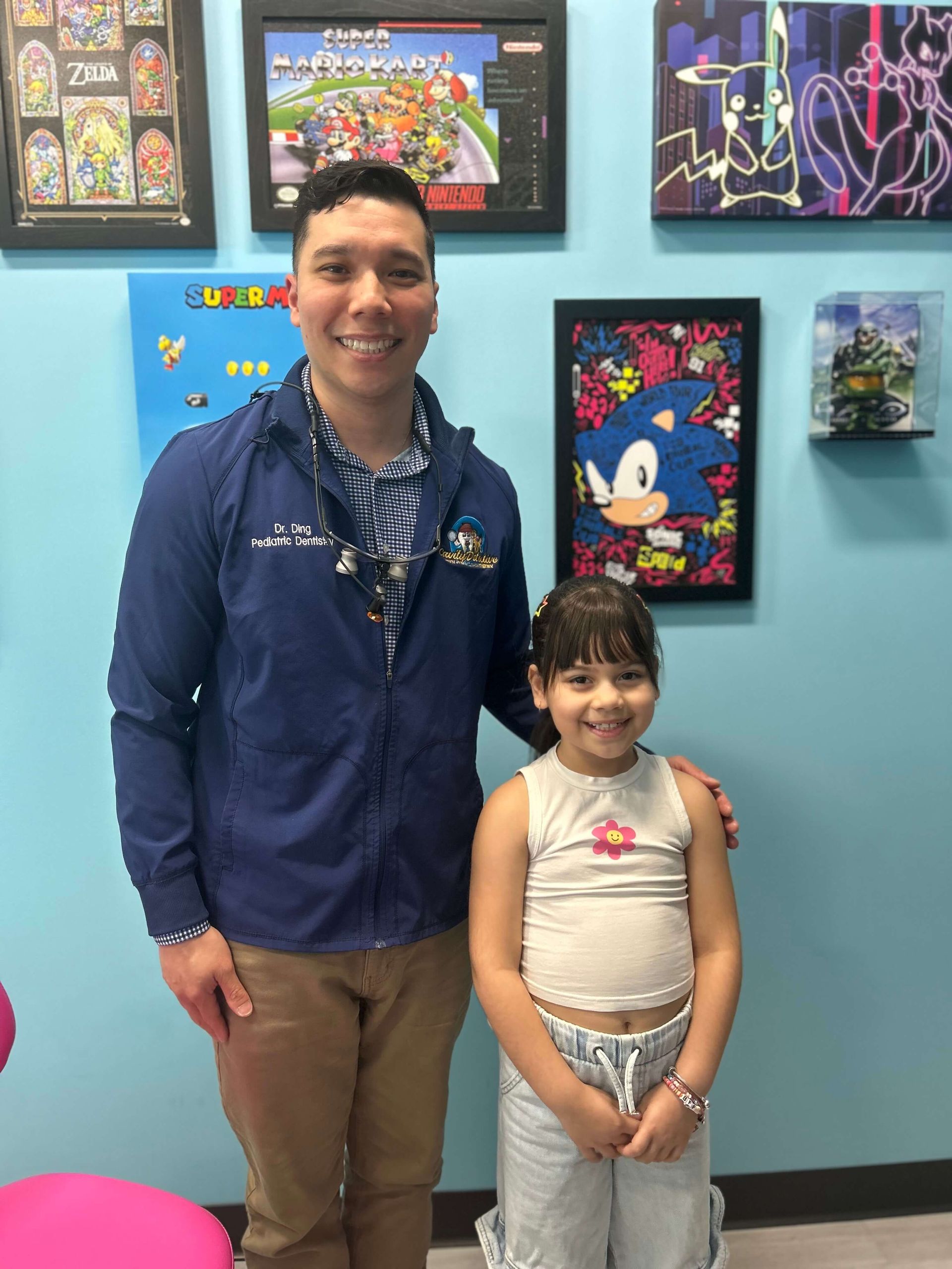 Two people smiling in a colorful gallery with framed cartoon artwork on a teal wall.
